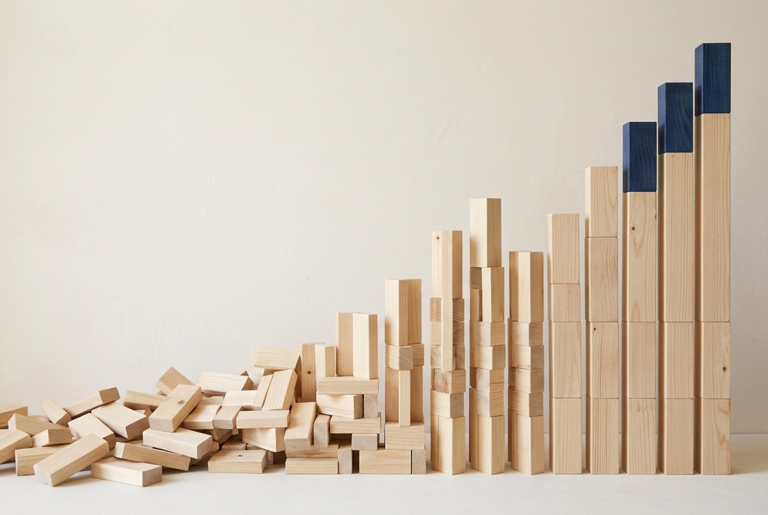 Blocks of pale timber on a plain wall, scattered at the left and standing in neat columns of rising height at the right, the tallest capped in deep blue.