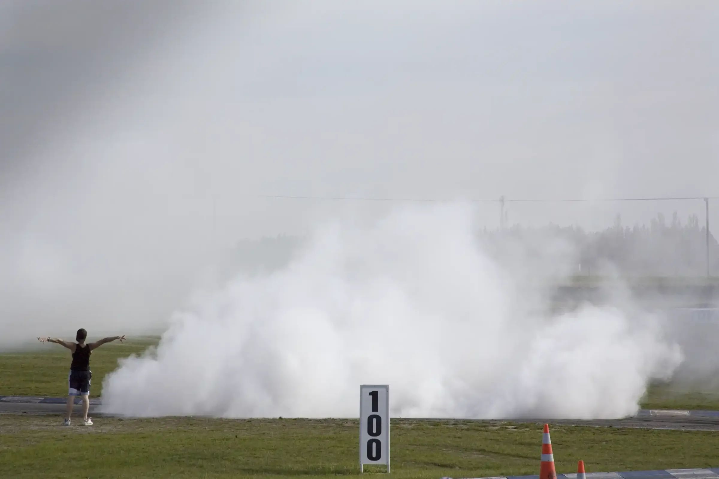 A cloud of tyre smoke drifting across a racetrack, one figure standing beside it.