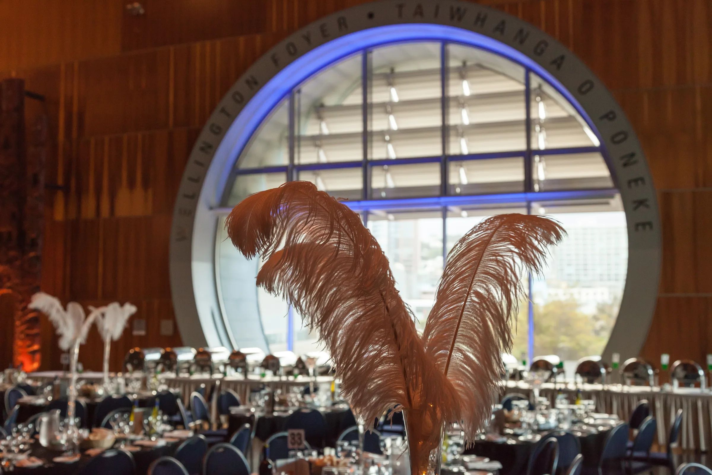 A function room set with long tables and tall vases of white feathers, before the guests arrive.