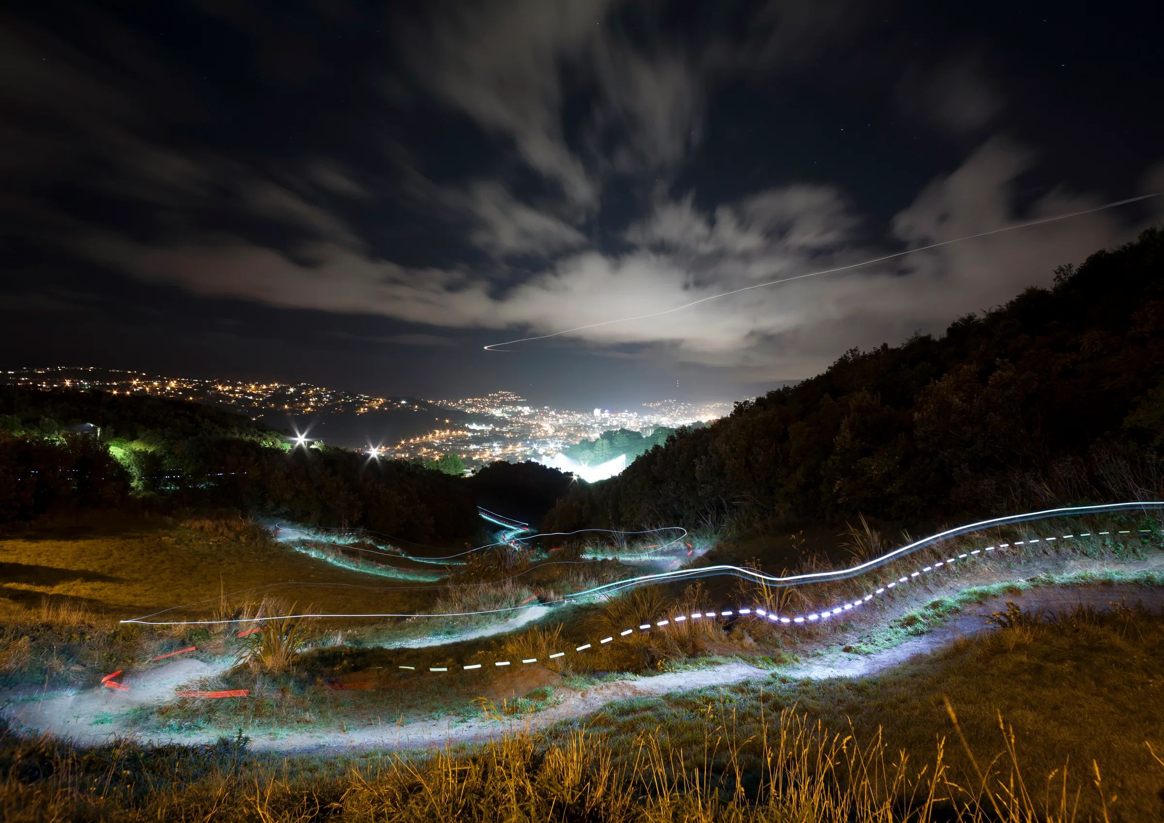 A ribbon of light tracing a mountain-bike trail over Mt Albert at night, with the lights of Wellington beyond.