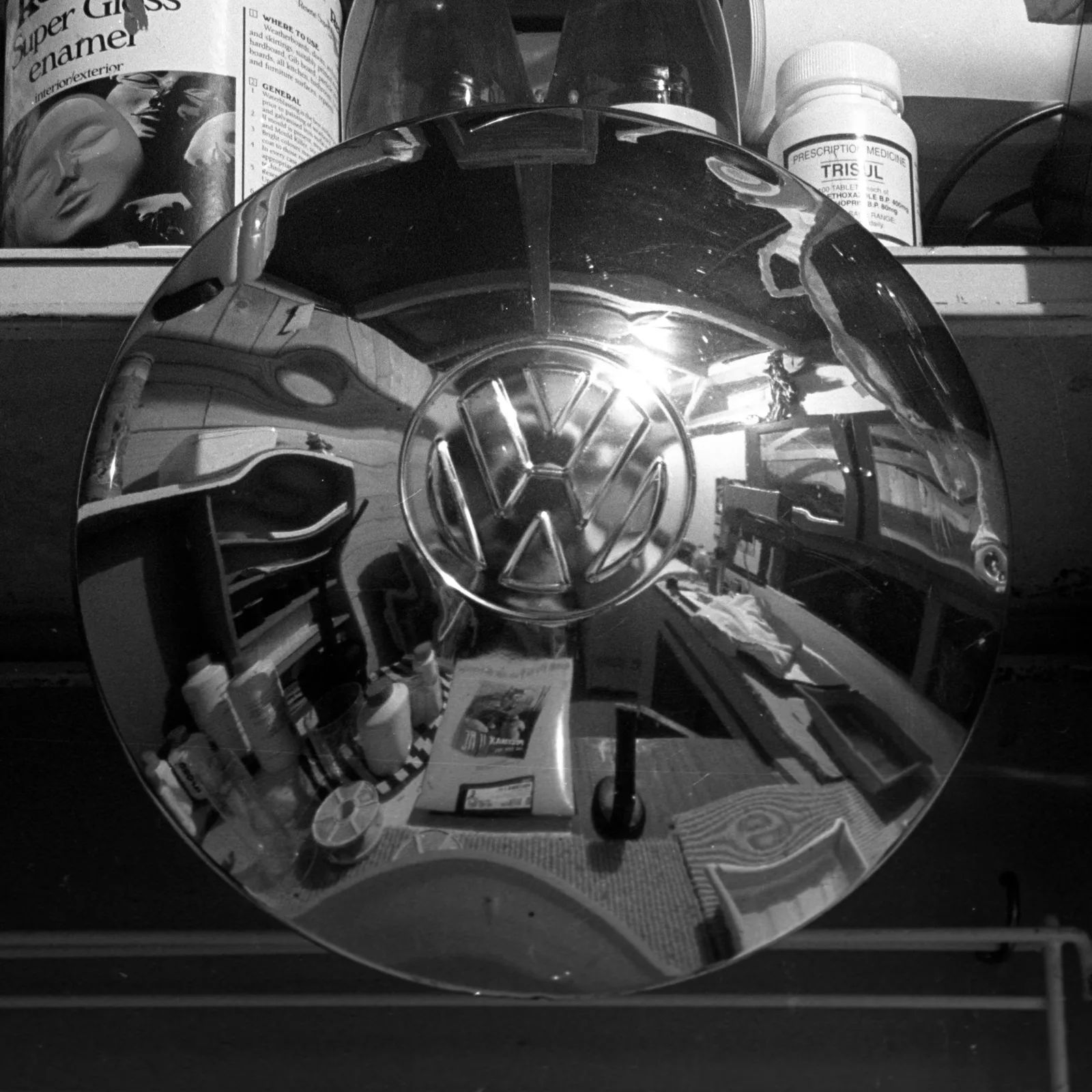 A chrome hubcap on a workshop shelf, reflecting the room around it, in black and white.